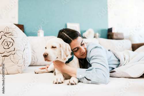 Young female owner sleeping in bed with labrador puppy.
