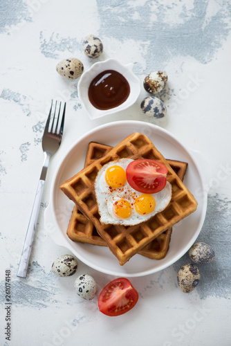 Belgian waffles and fried quail eggs, view from above on a white concrete background, vertical shot