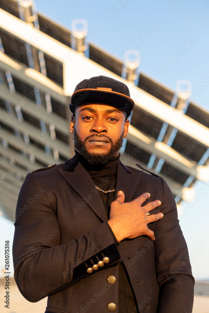 Front view of young black stylish man standing outdoors in a sunny day while looking camera