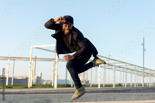 Stylish young male dancer in fashionable black clothes dancing blake dance on a street in the city on an autumn afternoon. Lifestyle.