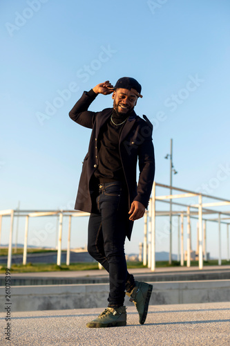 Front view of a black bearded man holding a hat while dancing and enjoying against blue sky in a sunny day