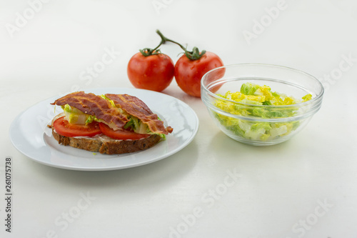 BLT sandwich on a white plate with lettuce and tomatoes on the side with a white background.