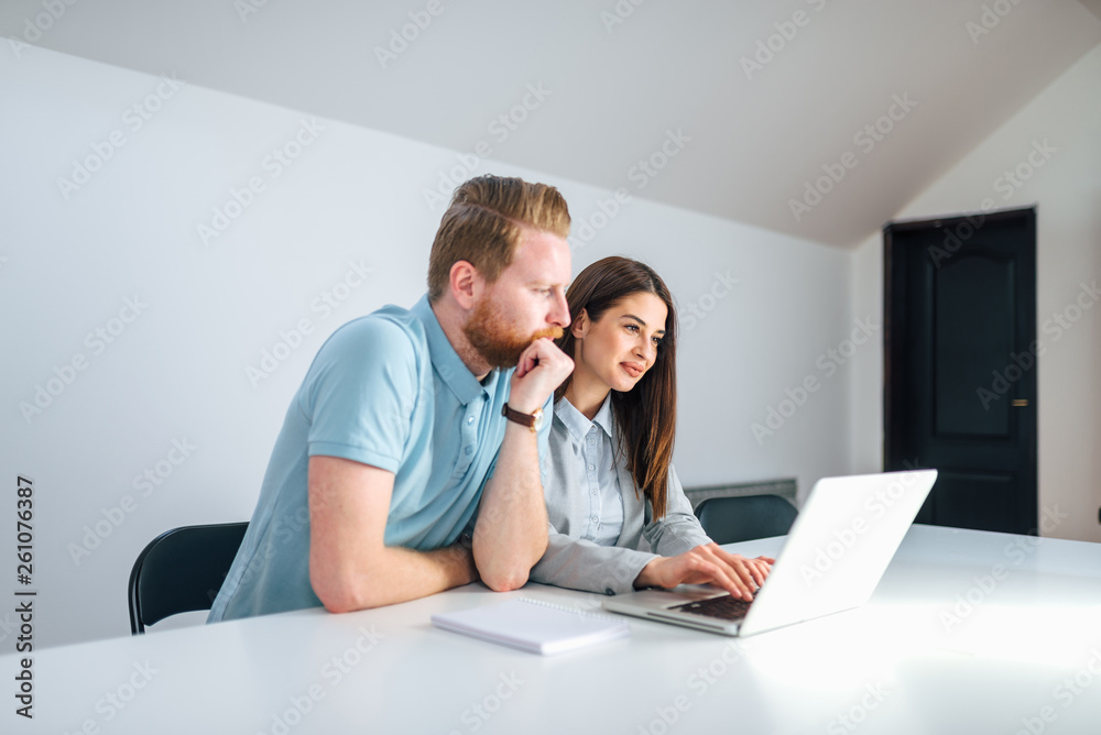 Two millenial entrepreneurs looking at laptop screen in a bright meeting room. Two millenial entrepreneurs looking at laptop screen in a bright meeting room.