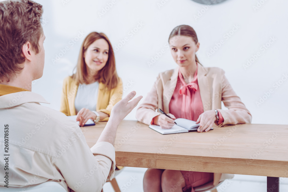 selective focus of man talking and gesturing near attractive recruiters on job interview selective focus of man talking and gesturing near attractive recruiters on job interview