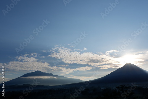 the view of the sun rises from behind the mountain, with a blue cloud background © andi