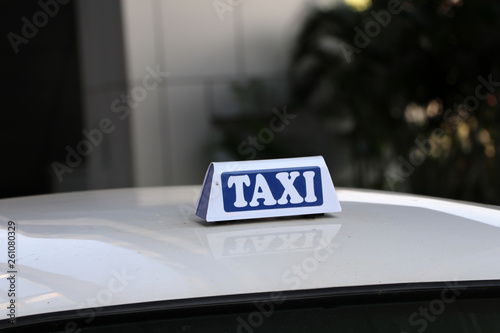 Taxi light sign or cab sign in white and blue color with white text on the car roof at the street blurred background.
