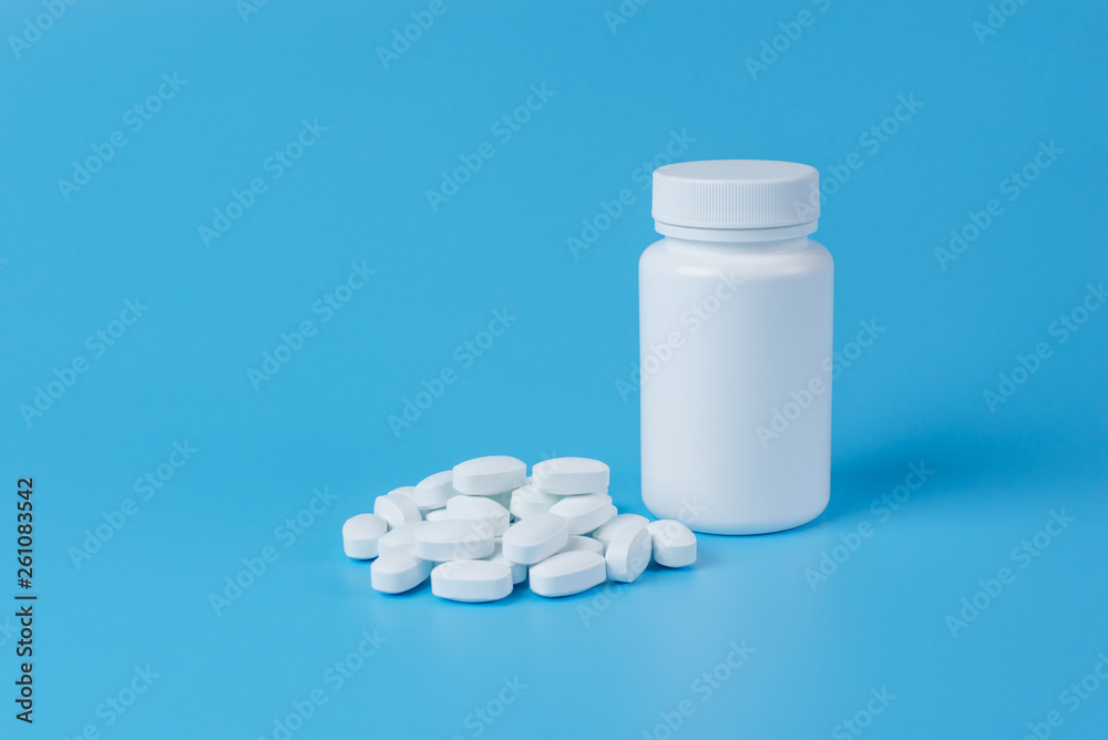 White pills, tablets and white bottle on blue background