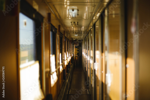 Long empty sunlit corridor of passenger train in warn colors. Train car interior. Concept of traveling and journey.
