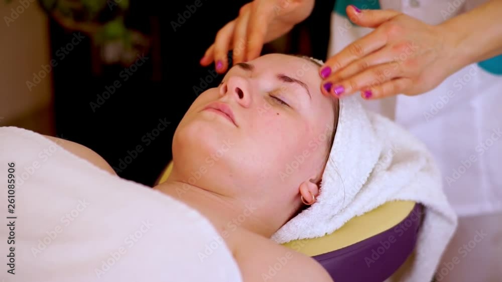 Hands of a cosmetologist in a circular motion massage the cheeks, eyebrows and forehead. The client lies relaxed on the couch. Hands of a cosmetologist in a circular motion massage the cheeks, eyebrows and forehead. The client lies relaxed on the couch.