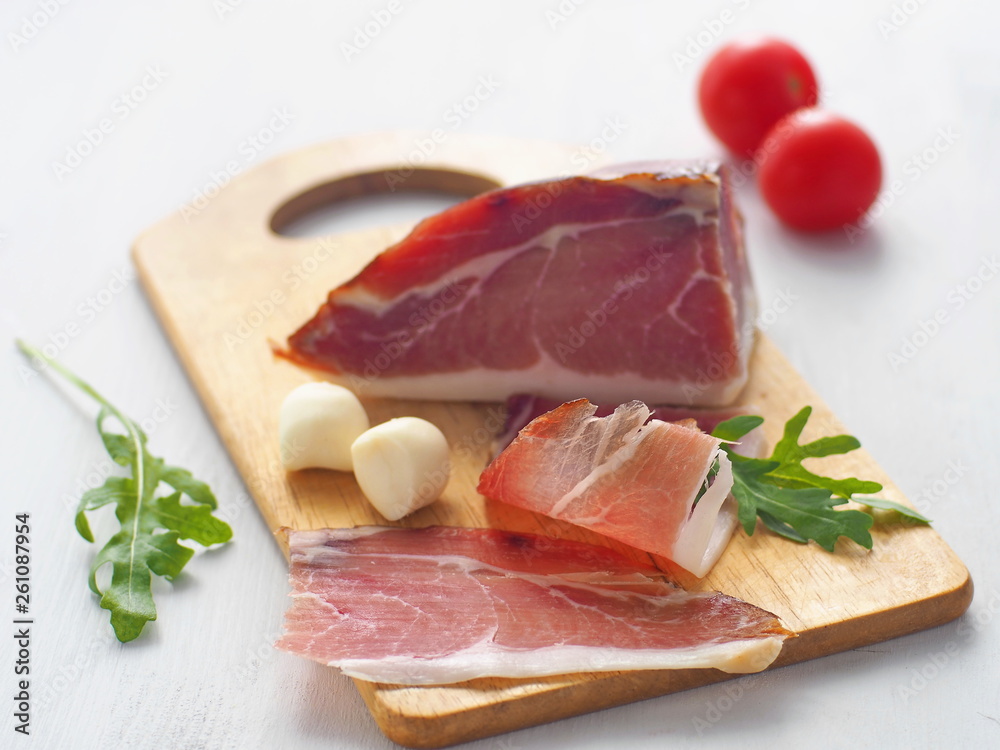 Fresh meat upon white table. Prosciutto, prsut, or Spanish jamon with cherry tomatoes, fresh arugula and mozzarella. Selective focus. Fresh meat upon white table. Prosciutto, prsut, or Spanish jamon with cherry tomatoes, fresh arugula and mozzarella. Selective focus.