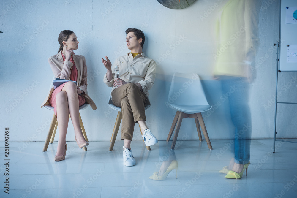 Obraz premium handsome employee with bottle of water sitting and talking with attractive woman