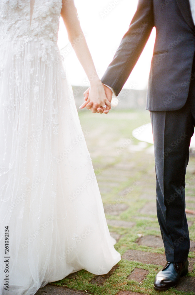 A bride & groom hold hands as golden sunset light pours through A bride & groom hold hands as golden sunset light pours through