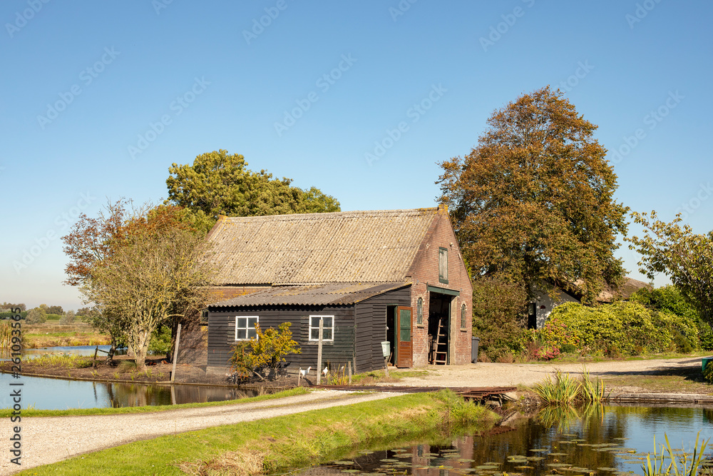 Old crooked barn surrounded by water in Dutch landscape.