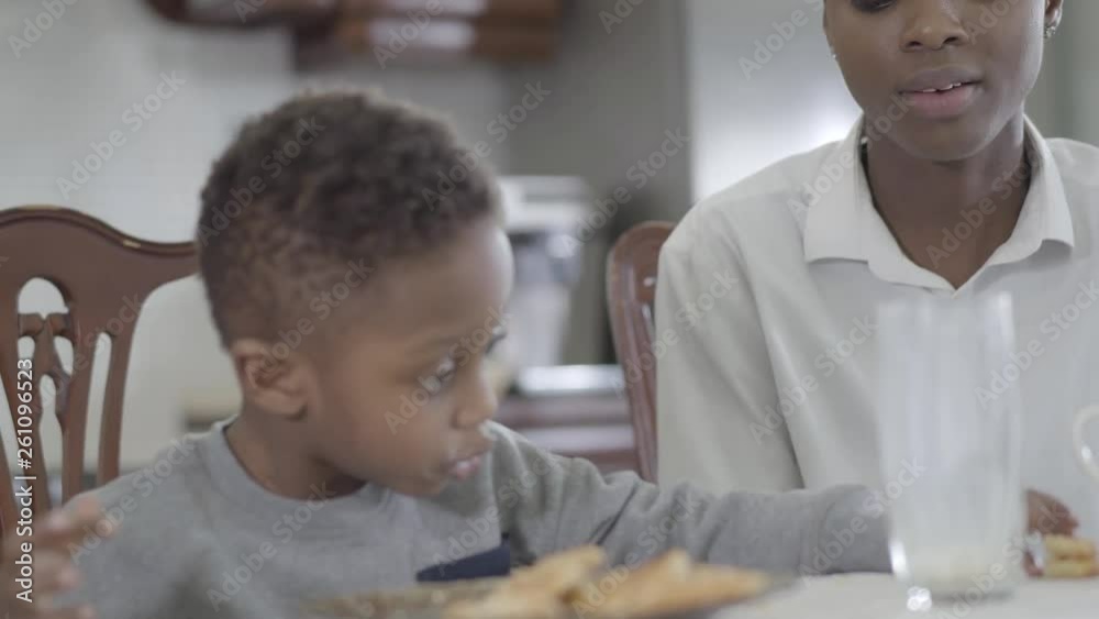 African american woman sitting with her little son by the table playing together with cookies. Family healthy breakfast. African american woman sitting with her little son by the table playing together with cookies. Family healthy breakfast.