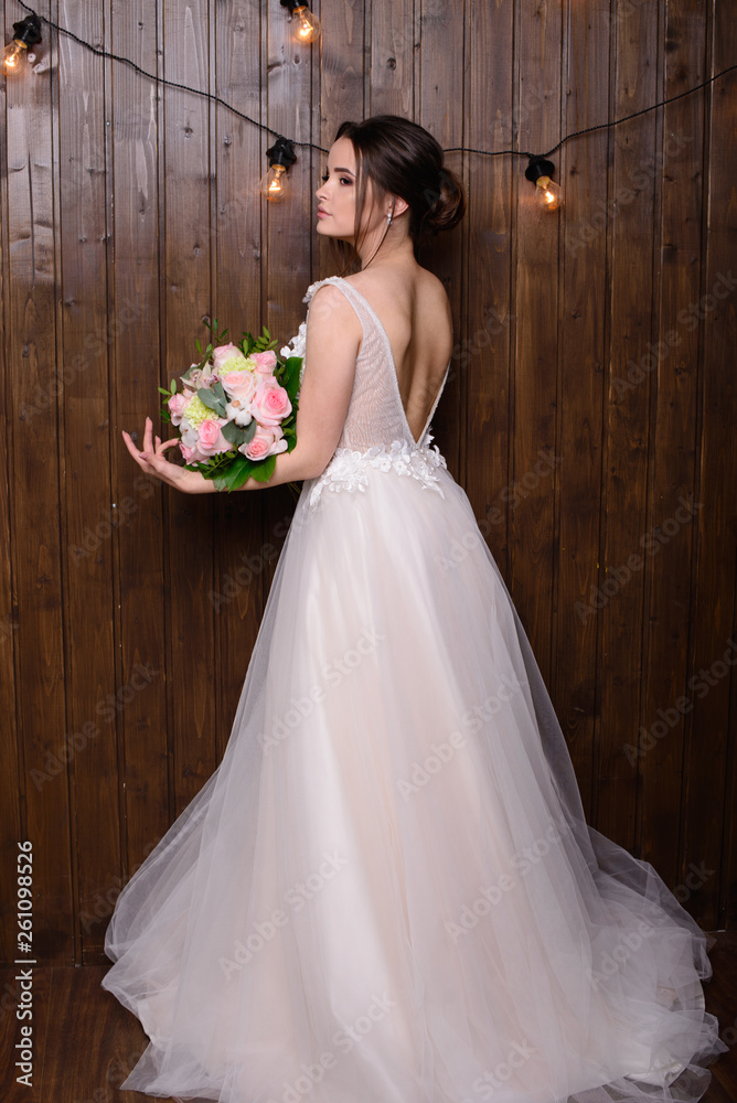 Slim beautiful woman wearing luxurious wedding dress on wooden background. Gorgeous bride holding flowers. Slim beautiful woman wearing luxurious wedding dress on wooden background. Gorgeous bride holding flowers.