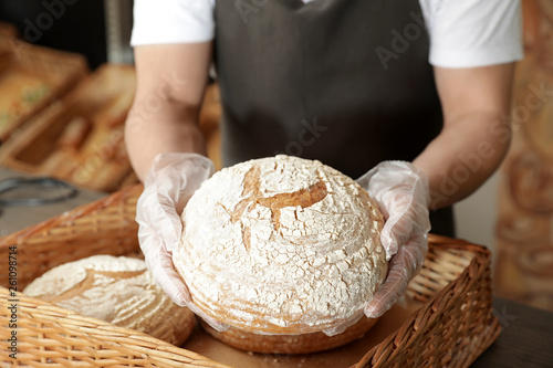 Professional baker holding loaf of bread over tray in store, closeup