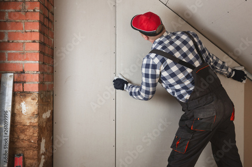 Obraz na plátně Man installing plasterboard sheet to wall for attic room construction