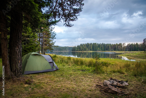 Camping near a lake in a cloudy day - tent and a fireplace near a lake. 