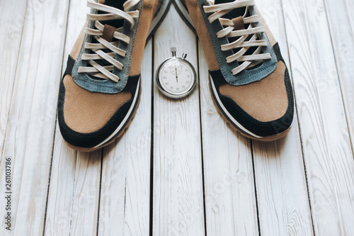 Pair of beige sport shoes (sneakers) from suede with stopwatch on white rustic wooden background. Training, jog and sport concept. Close up. photo