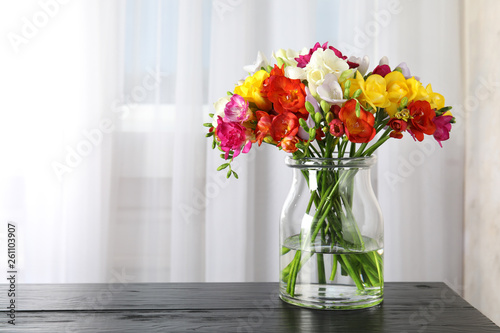 Vase with bouquet of spring freesia flowers on table in room. Space for text