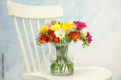 Beautiful bright freesia flowers in vase on chair
