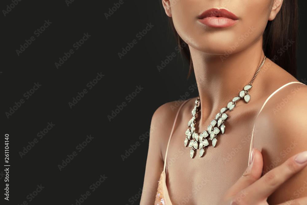 Beautiful young woman with elegant jewelry on dark background, closeup. Space for text