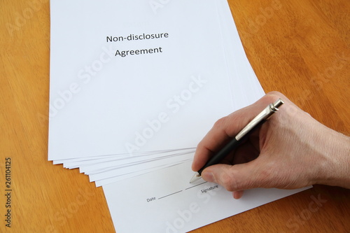 Non-disclosure agreement and hand with pen about to sign it on wooden table