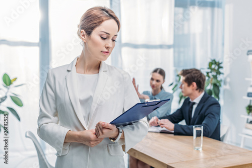 selective focus of attractive recruiter standing with clipboard near coworkers