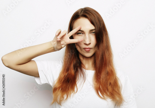 Portrait of gorgeous woman looking at camera with smile and showing peace sign with fingers