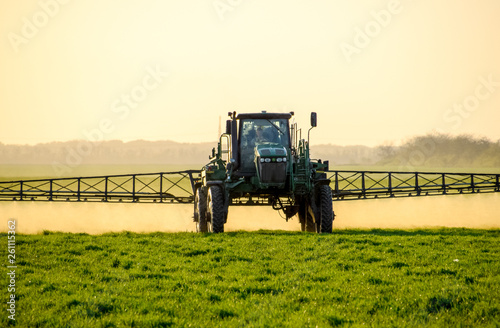 Tractor on the sunset background. Tractor with high wheels is making fertilizer on young wheat. The use of finely dispersed spray chemicals