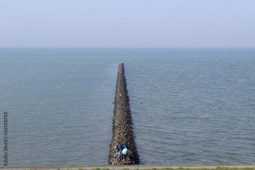 Fototapeta premium Opposites: the water breaks on one side, the other is quiet with running water in the Wadden Sea