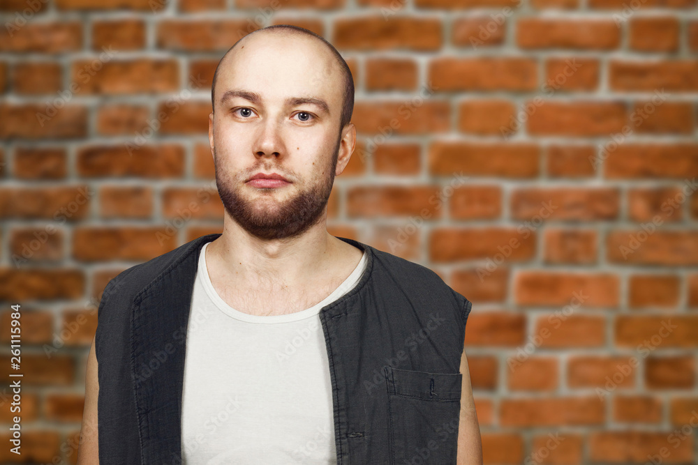Portrait Young bald guy with beard with pocker face dressed in sleeveless shirt. Man on brick. wall background. Portrait Young bald guy with beard with pocker face dressed in sleeveless shirt. Man on brick. wall background.