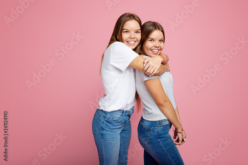 Bright two young twin sisters with beautiful smile walk over pink background.