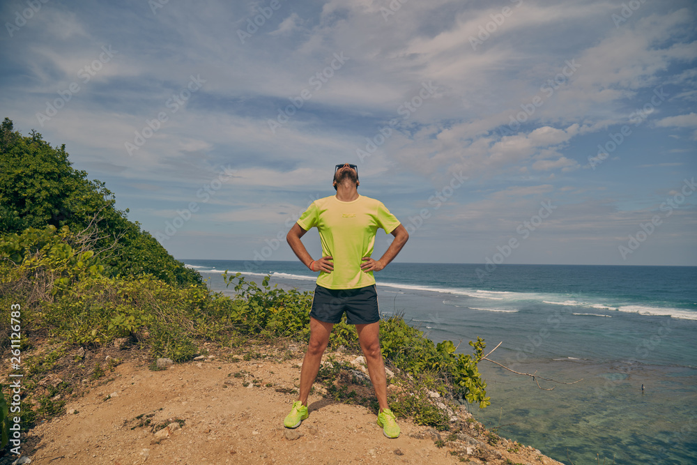 Sportsman stretching on a tropical exotic cliff near the ocean.