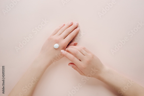 Woman moisturizing her hand with cosmetic cream lotion with copy space on beige background. Concept template feminine blog, beauty concept