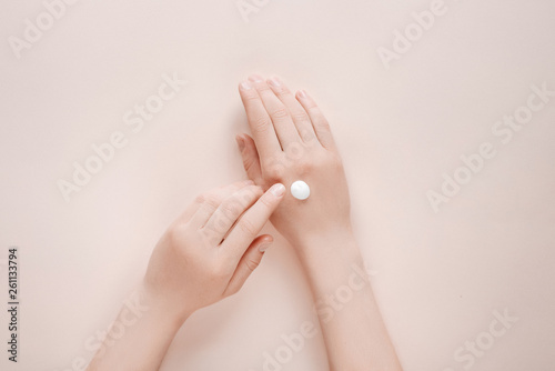 Woman moisturizing her hand with cosmetic cream lotion with copy space on beige background. Concept template feminine blog  beauty concept