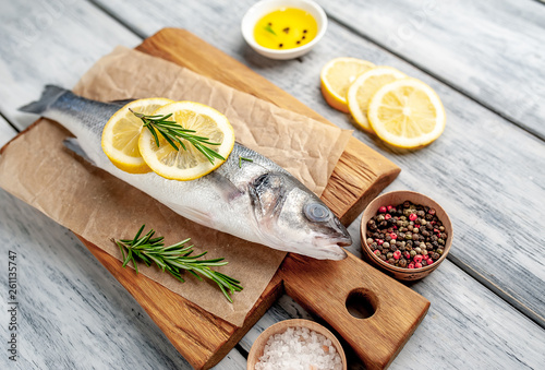 chilled raw sea bass fish with ingredients on a cutting board on a wood background