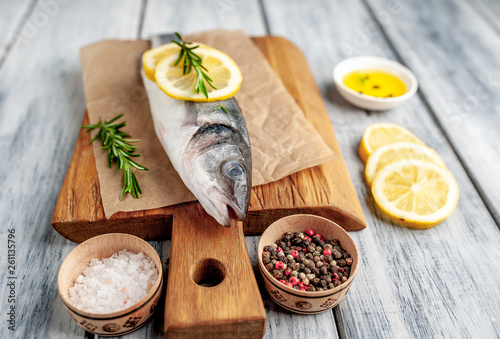chilled raw sea bass fish with ingredients on a cutting board on a wood background
