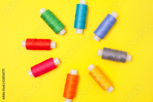 Set of multicolored spools of thread on yellow background. Accessories for needlework, embroidery, sewing. Flat lay. Top view. Objects are located in center, forming flower.