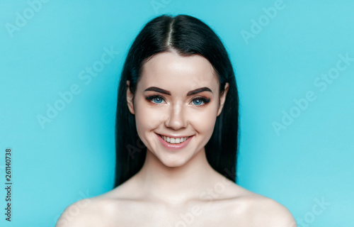 Portrait of model with natural nude make up with bare shoulders on blue background. Beautiful young woman with perfect glow clean skin. Skincare, cosmetology, beauty, fashion concept. Blue eyes. photo