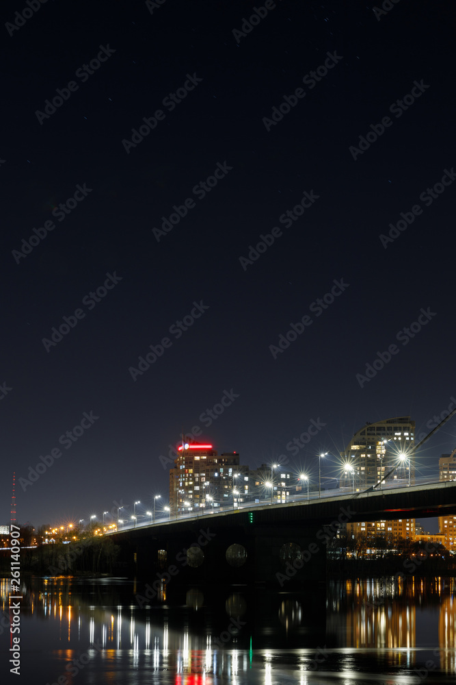 dark cityscape with illuminated buildings, lights, bridge and river