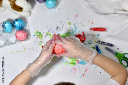 Children's hands are painting eggs in red on the working surface.
