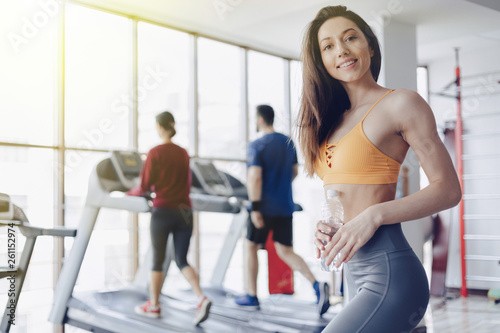 young attractive girl in the gym drinking water on the background of treadmills
