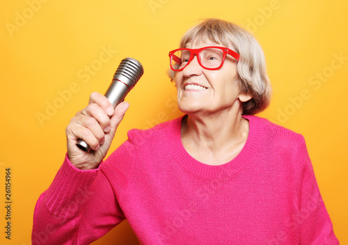 Portrait of funny grandmother holds up the microphone stand and sings isolated on vivid yellow background