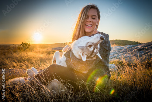 Woman laughs while snuggling her husky dog sitting on an open ridge with the sun rising behind her. photo