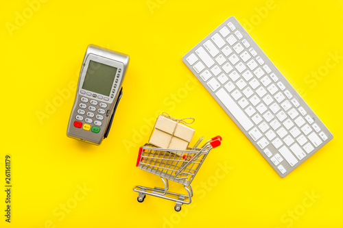 making purchase online with card machine, keyboard and mini trolley on yellow desk background top view