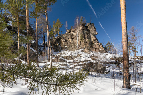 Picturesque rocks against the blue sky in the snow covered winter pine forest, Siberian taiga, the Baikal region, Irkutsk region, Russia