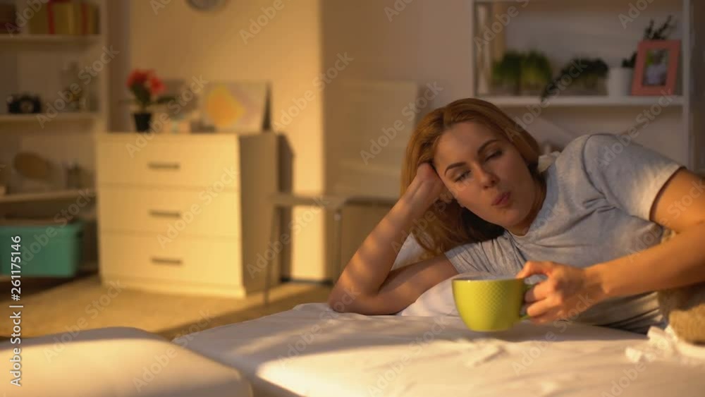 Relaxed happy woman drinking coffee lying in bed, rest on weekend morning, peace