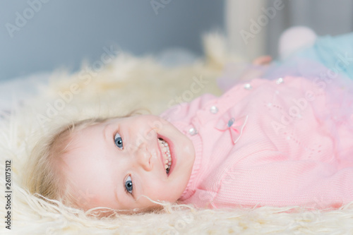Little girl in a pink jacket lying on the bed and smiling