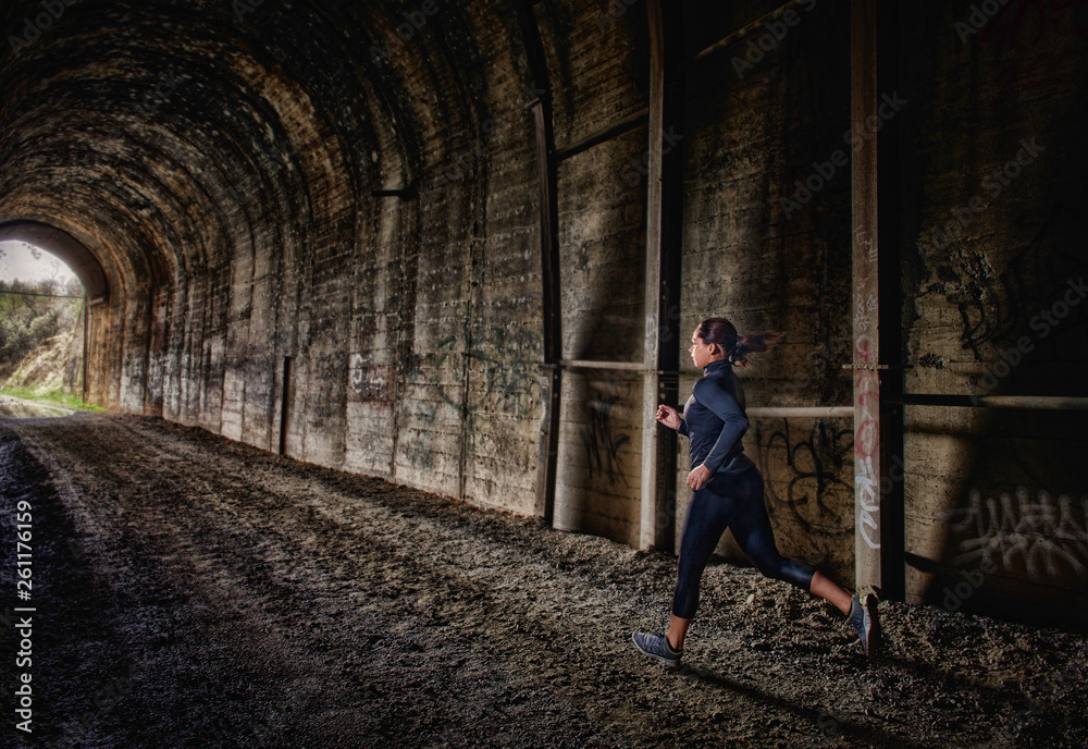 A young woman running through a tunnel as part of her morning fitness routine. A young woman running through a tunnel as part of her morning fitness routine.